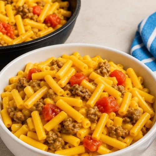 Easy 20 Minute Cheeseburger Mac and Cheese served in a white bowl with a skillet of cheesy beef pasta in the background.