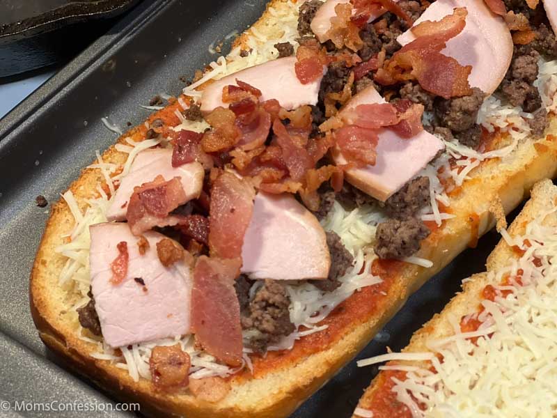 close up of meat lovers french bread pizza on a baking sheet