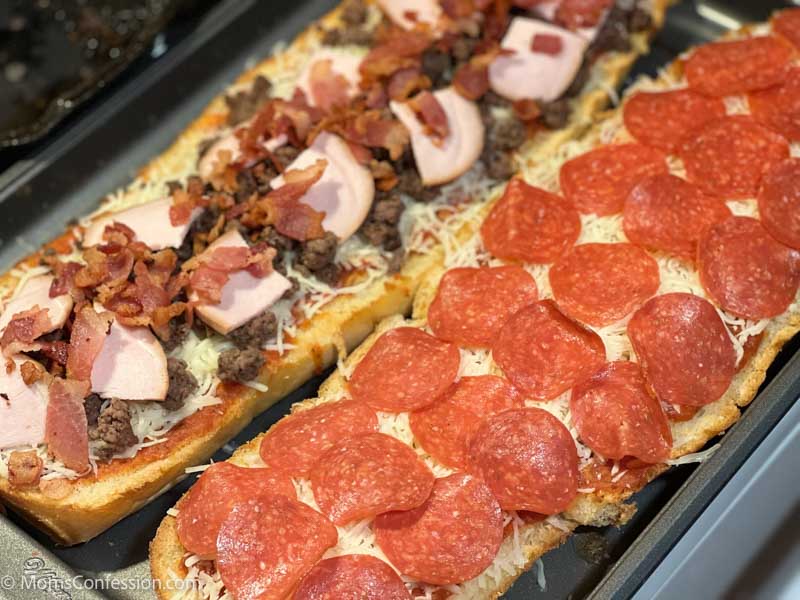 overhead photo of meat lovers and pepperoni french bread pizza on a baking sheet
