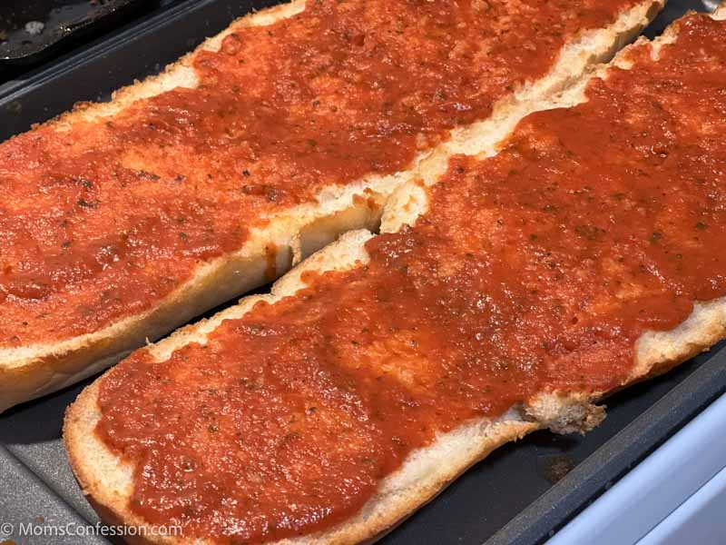 french bread with pizza sauce on a baking sheet