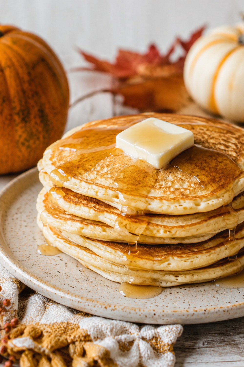 Stack of fluffy pumpkin pancakes with melted butter and maple syrup surrounded by pumpkins and fall decor