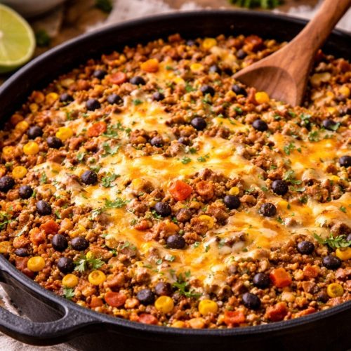 One pot taco rice skillet with ground beef, rice, black beans, corn, and melted cheddar cheese in a cast iron skillet.