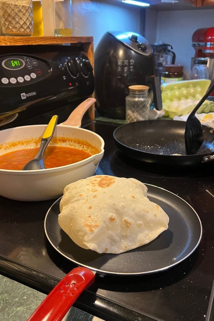 Homemade flour tortilla puffing in a skillet while cooking on the stovetop.