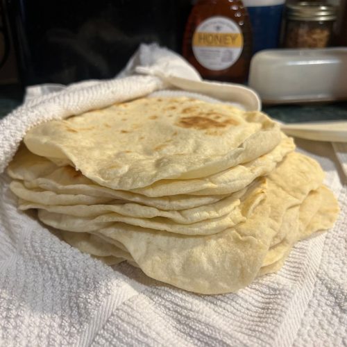 Freshly made homemade flour tortillas stacked on a towel to stay warm and soft.