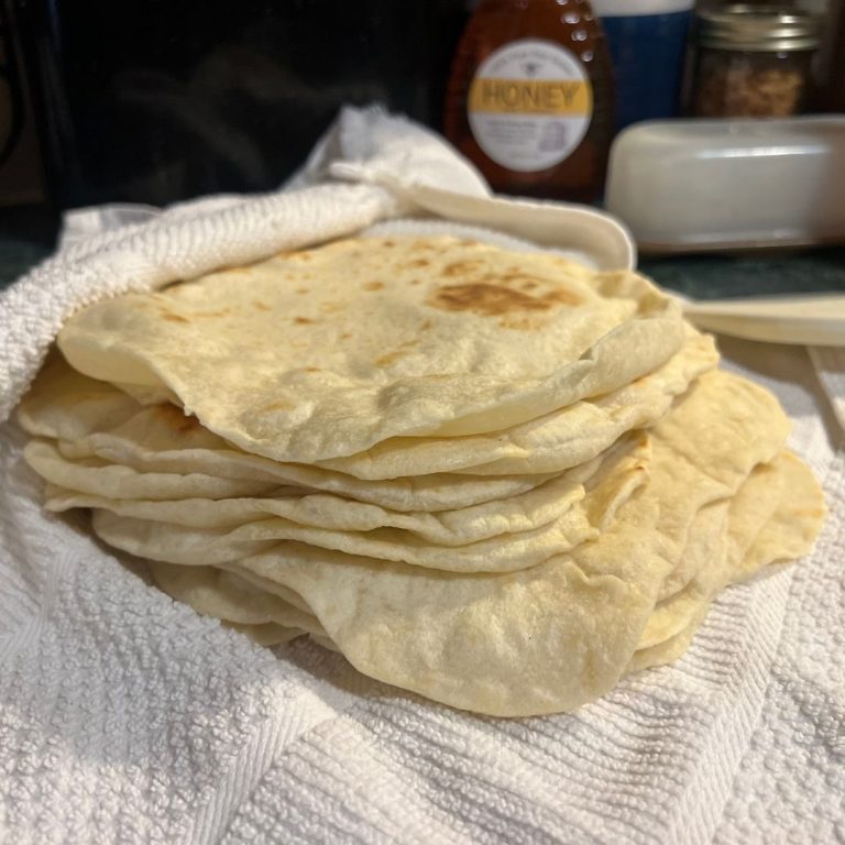 Freshly made homemade flour tortillas stacked on a towel to stay warm and soft.